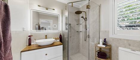 A modern bathroom with a glass-enclosed shower, a white sink, and a vanity with drawers.
