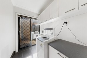 A modern kitchen with a built-in washing machine, a countertop, and a sliding glass door leading to a patio. - Family 3-Bed Retreat in Point Cook (Point Cook)