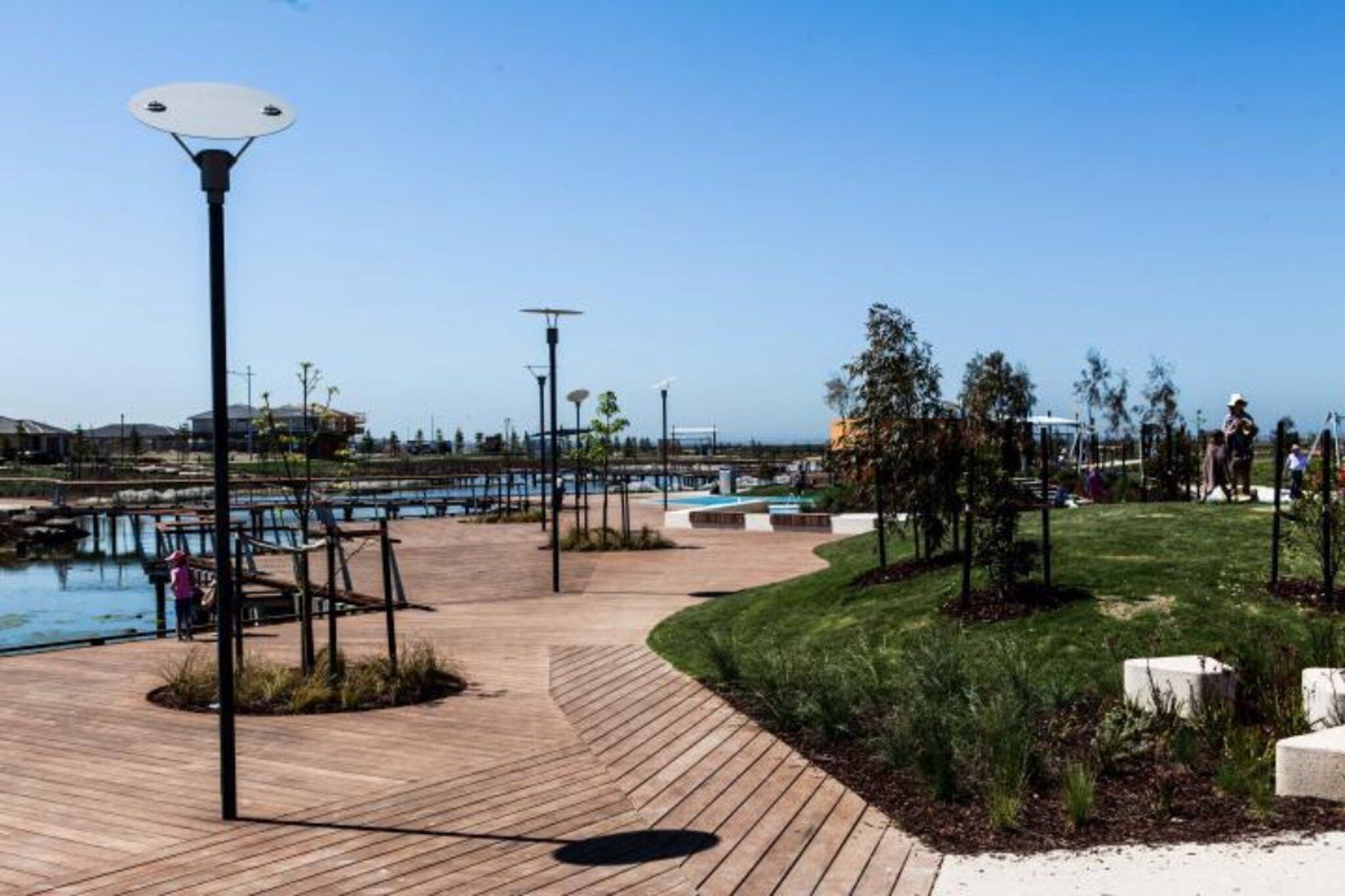Une promenade en bois mène à un espace piscine agrémenté de lampadaires et d’arbres.