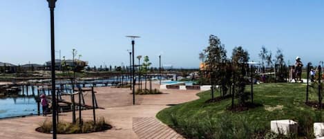 A wooden boardwalk leading to a pool area with lamp posts and trees.