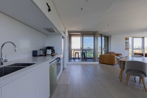 A modern kitchen with a built-in oven and a dining area with a table and chairs. - Skyline-View 2-Bed Apartment Near Flemington (Flemington)
