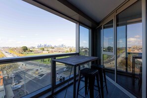 Ein Balkon mit Tisch und zwei Stühlen, mit Blick auf eine Stadtlandschaft mit Gebäuden und einer Straße.