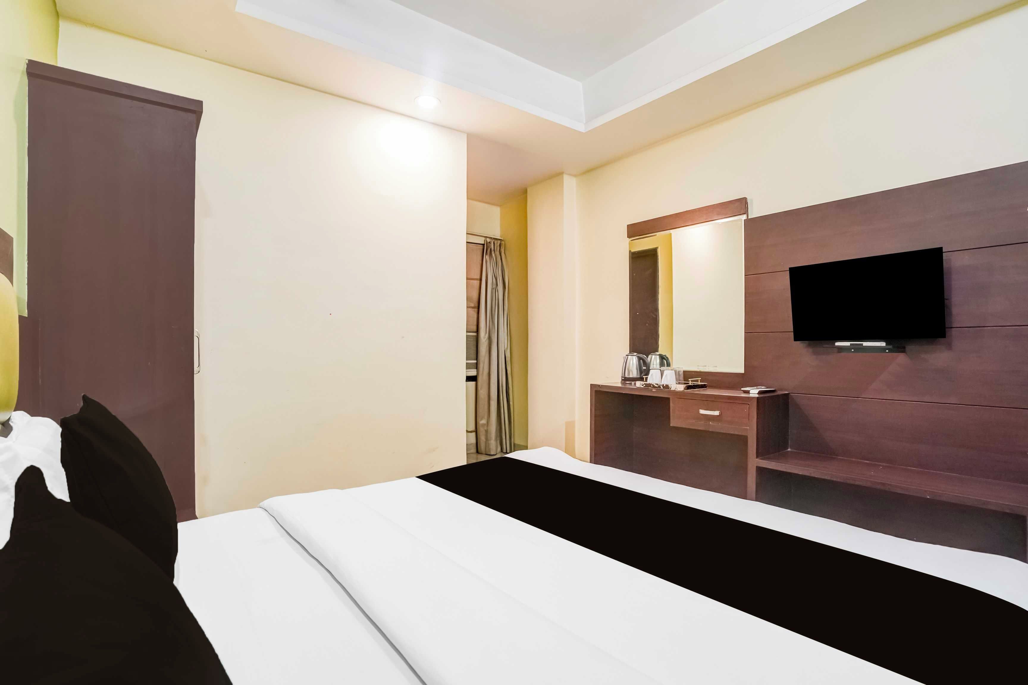 A hotel room with a bed, a bedside table, a mirror, a television, and a shower area.