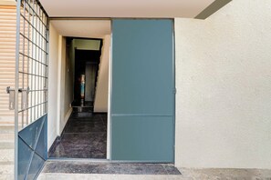 Um corredor estreito com um portão de metal à esquerda e uma porta azul à direita.