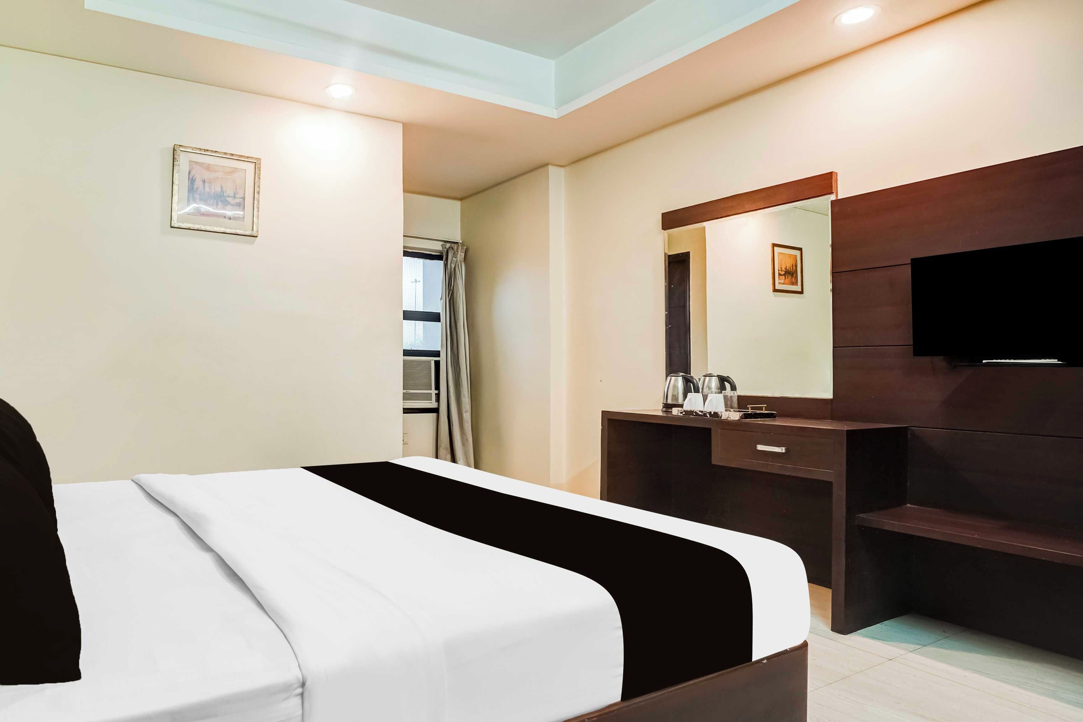 A hotel room with a bed, a dresser, a mirror, a television, and a window with curtains.