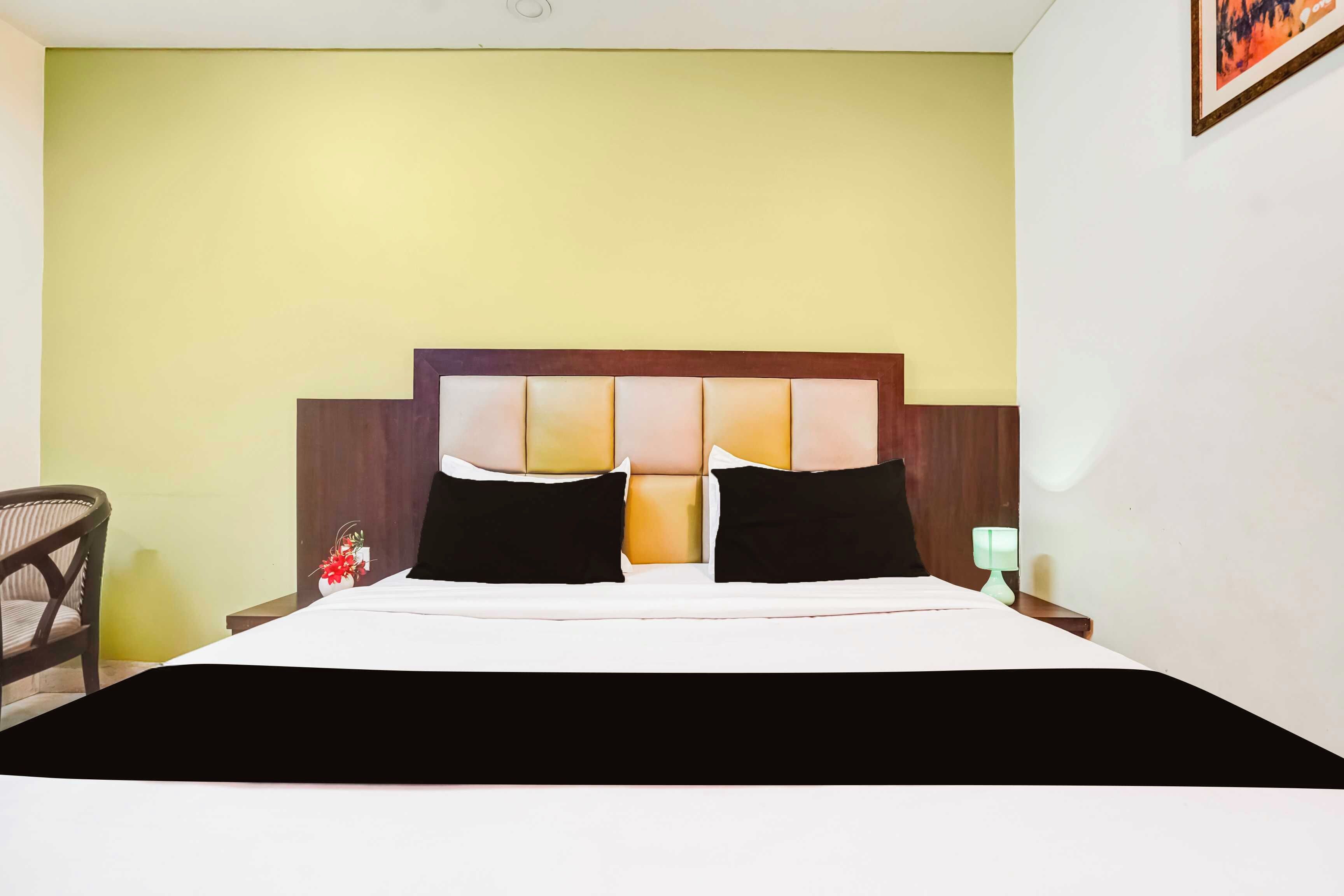 Une chambre d’hôtel avec un lit, une table de chevet, une chaise et une lampe fixée au mur.