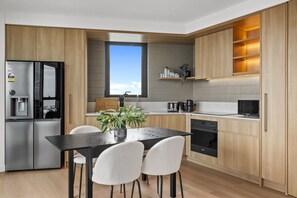 A modern kitchen with a built-in refrigerator, a dining table with chairs, and a window above the sink. - Light-Filled 3-Bed Brand New Apartment (St Kilda)