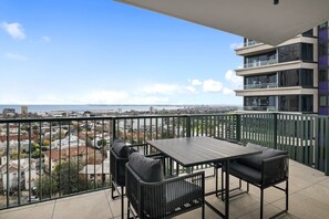 A balcony with a table and chairs, overlooking a cityscape and the sea. - Light-Filled 3-Bed Brand New Apartment (St Kilda)