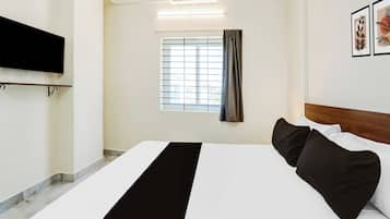 Une chambre d’hôtel avec un lit, un téléviseur à écran plat fixé au mur, une fenêtre avec des rideaux et des œuvres d’art encadrées accrochées au mur.