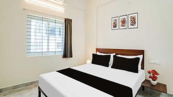 A hotel room with a bed, a window with curtains, a nightstand with a lamp, and a wall with framed artwork.