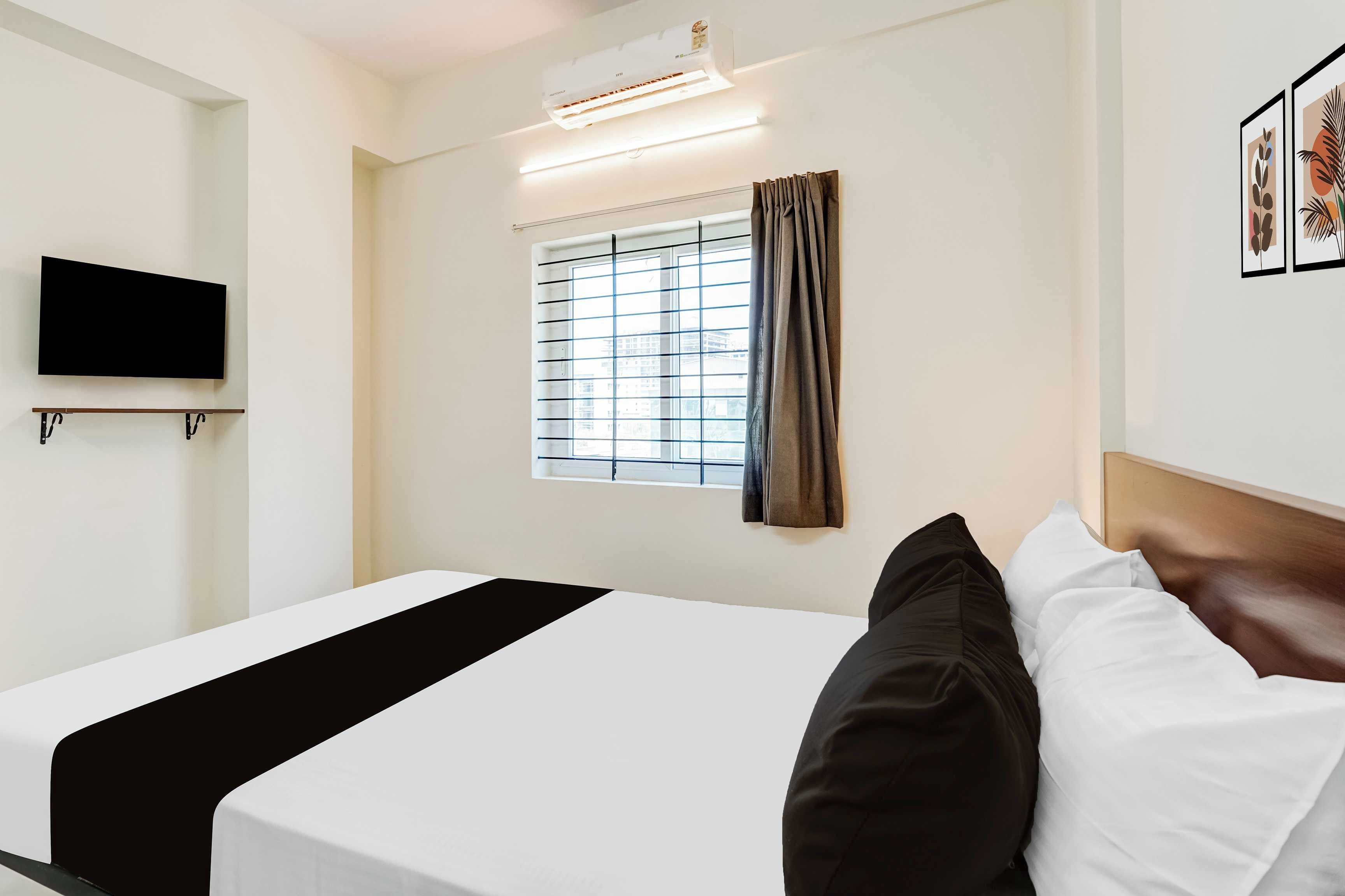 Una habitación de hotel con cama, televisor montado, ventana con persianas y aire acondicionado instalado en la pared.