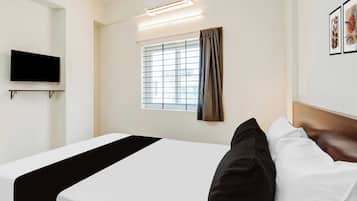 Una habitación de hotel con cama, televisor montado, ventana con persianas y aire acondicionado instalado en la pared.