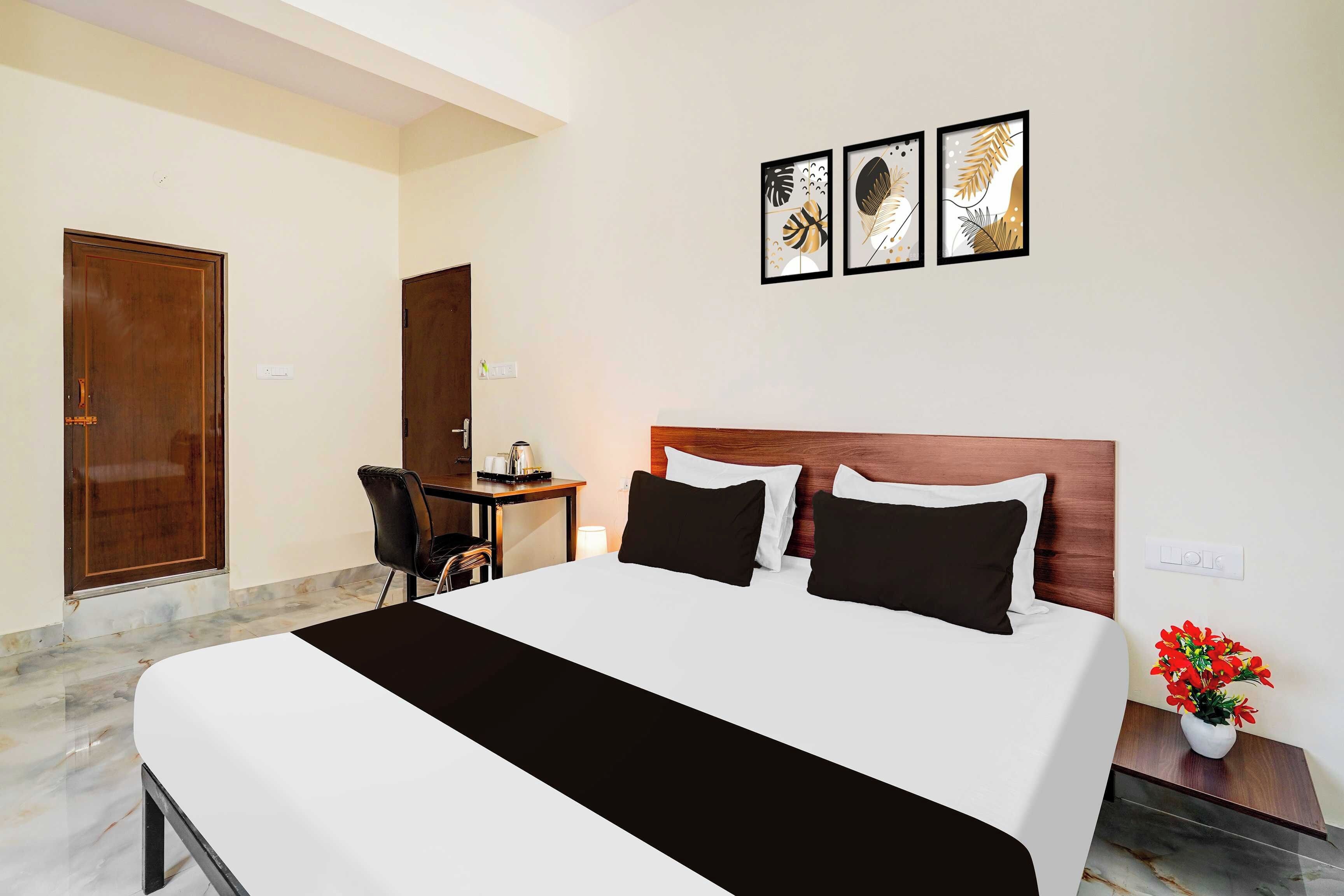 A hotel room with a bed, a desk, and a chair. There are three framed pictures on the wall.