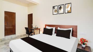 A hotel room with a bed, a desk, and a chair. There are three framed pictures on the wall.