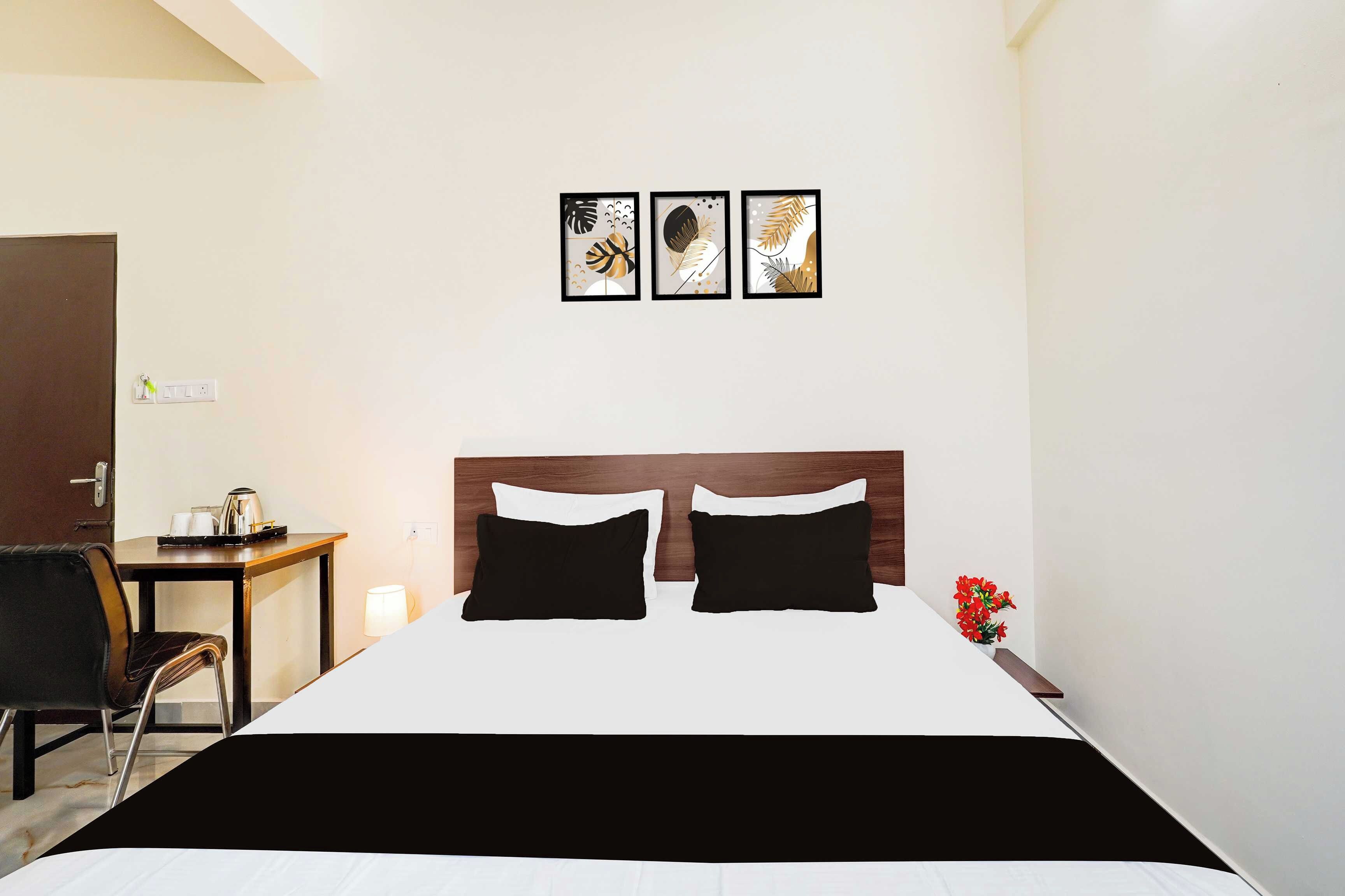 A hotel room with a bed, a desk, a chair, and three framed artworks on the wall.