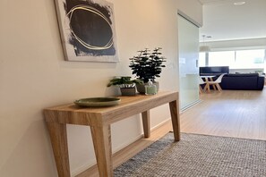 A wooden console table with a bowl and a potted plant, a framed artwork above it, and a view into a living area with a sofa and a TV. - Stylish 1-Bed Apartment in Adelaide CBD (Adelaide)