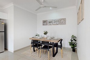 Ein Essbereich mit Tisch für vier Personen, schwarzen Stühlen, Deckenventilator und Wandbild.