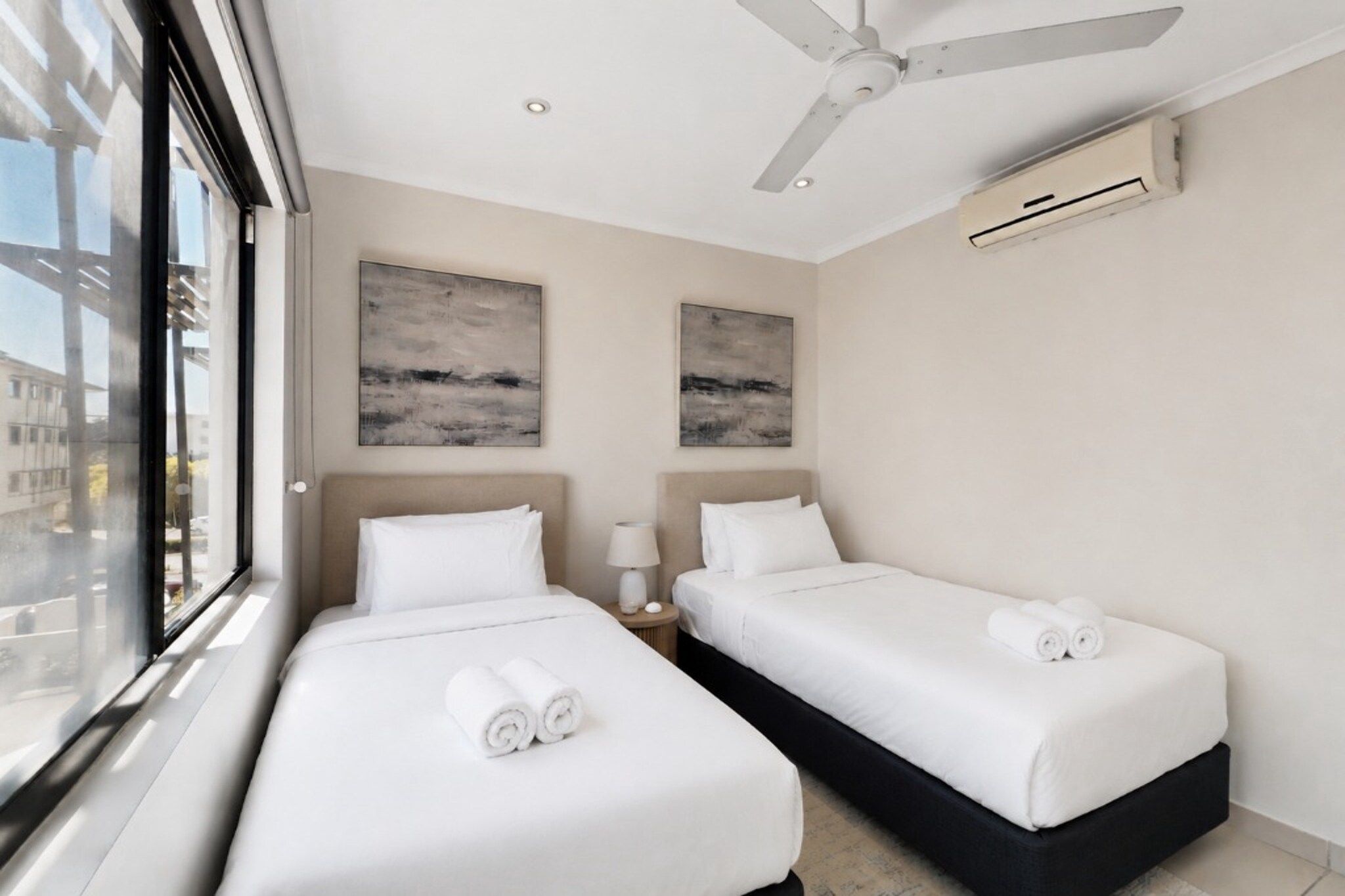 Une chambre d’hôtel avec deux lits, un ventilateur de plafond et des œuvres d’art accrochées aux murs.