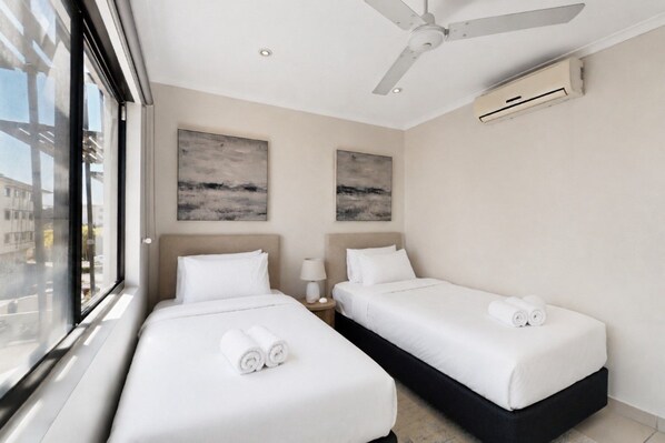 A hotel room with two beds, a ceiling fan, and artwork on the walls.