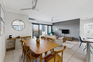 A modern living room with a dining area, a flat-screen TV mounted on the wall, and a ceiling fan.