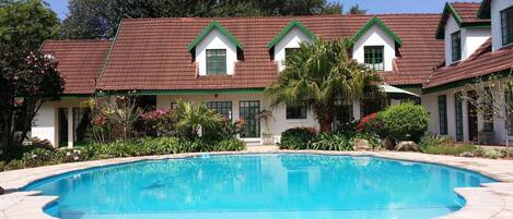 Una piscina rodeada por una casa con techo de tejas rojas y detalles en verde.