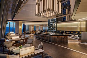 Un moderno vestíbulo de hotel con zona de bar, arreglos de asientos y vista panorámica de la ciudad.