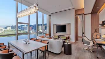 Habitación de hotel moderna con televisor grande, zona de estar y vistas a un paisaje urbano.