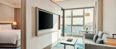 Habitación de hotel moderna con cama, televisor de pantalla plana, sofá, mesa de centro y un amplio ventanal con vistas.