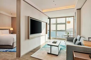 Habitación de hotel moderna con cama, televisor de pantalla plana, sofá, mesa de centro y un amplio ventanal con vistas.
