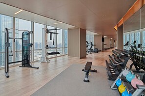 Un gimnasio moderno con equipamiento de ejercicio, ventanas amplias y vistas a la ciudad.