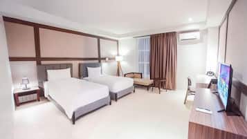 Ein Hotelzimmer mit zwei Betten, einem Schreibtisch, einem Sessel, einem Fernseher und einem Fenster mit Vorhängen.