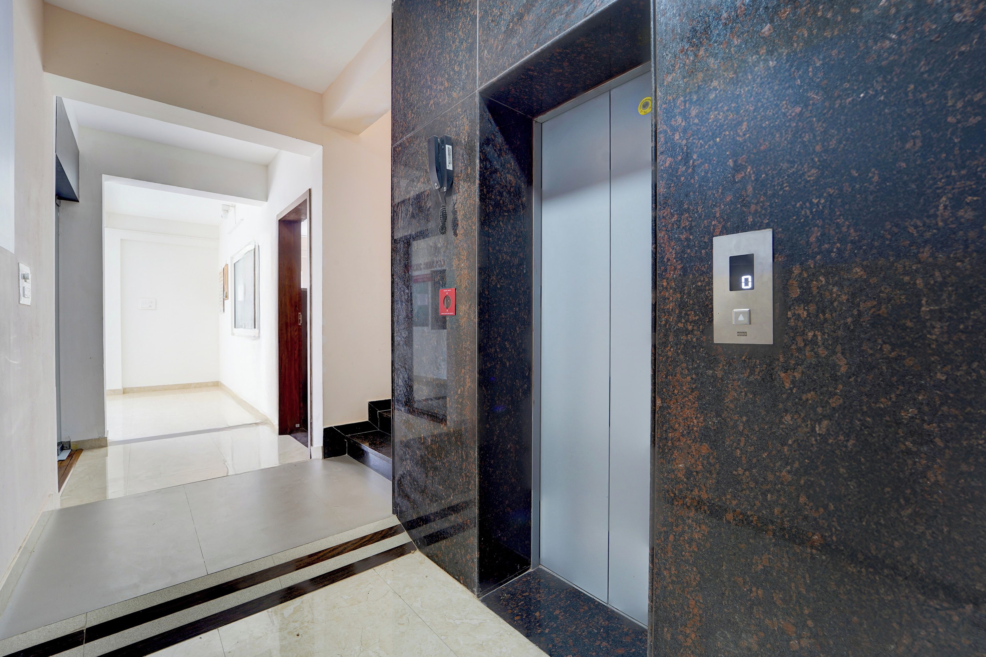 A hallway with a marble floor, a door, and an elevator with a digital display.