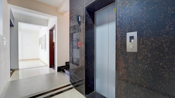 A hallway with a marble floor, a door, and an elevator with a digital display.