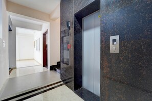 Um corredor com piso de mármore, uma porta e um elevador com visor digital.