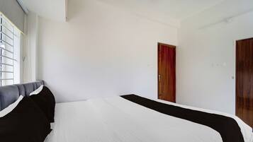 Quarto com cama, janela com persianas, porta e interruptor de luz na parede.