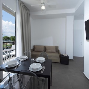 A modern dining area with a table set for four, a sofa, and a balcony with a view. - Hotel Niagara (Cattolica)