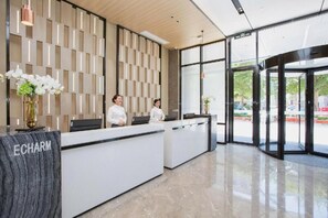 A reception area with a modern design, featuring a reception desk, a wall with a geometric pattern, and a glass entrance. - Echarm Hotel (Shenzhen)