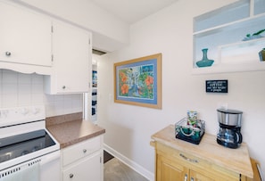 A kitchen with white cabinets, a stove, a coffee maker, and a framed painting on the wall. - Pet Friendly 2BR Fenced-In near St. Pete Beach (St. Petersburg)