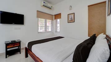 Um quarto com uma cama, uma TV, uma mesa de cabeceira e uma janela.