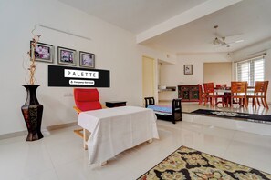 A hotel room with a bed, a dining area with chairs, a table, and artwork on the wall.