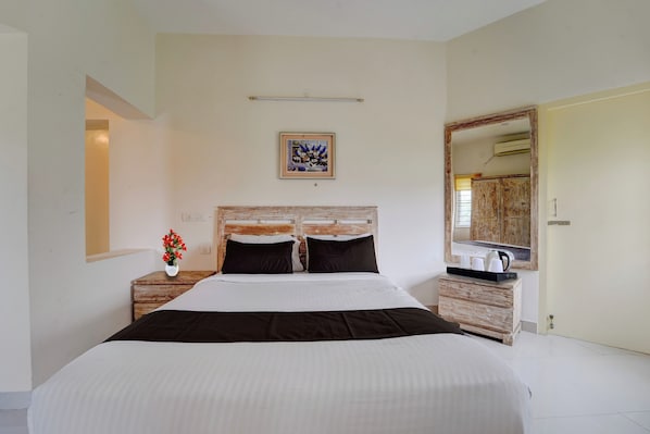 A bedroom with a large bed, a bedside table with a vase of flowers, a framed picture on the wall, and a mirror above the door.