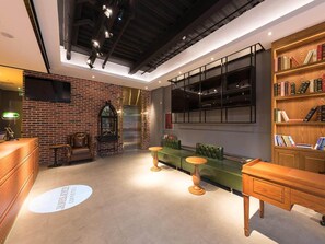 A modern interior with a brick wall, a green sofa, a wooden bookshelf, and a reception desk. - James Joyce Coffetel (Beijing)