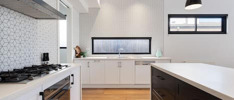 A modern kitchen with white cabinetry, a large window, and a geometric backsplash.