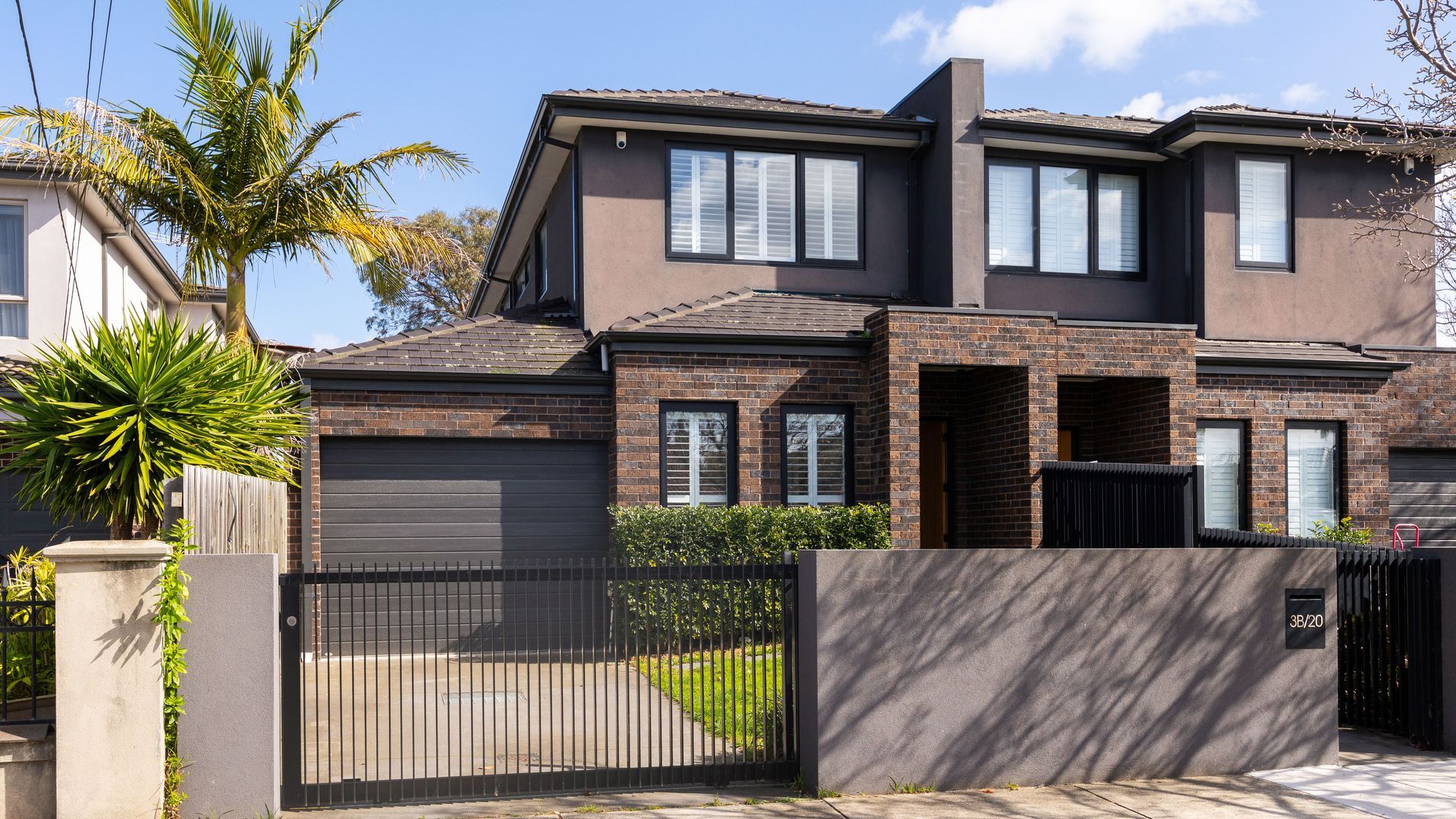 A modern two-story house with a brick facade, large windows, and a gated driveway.