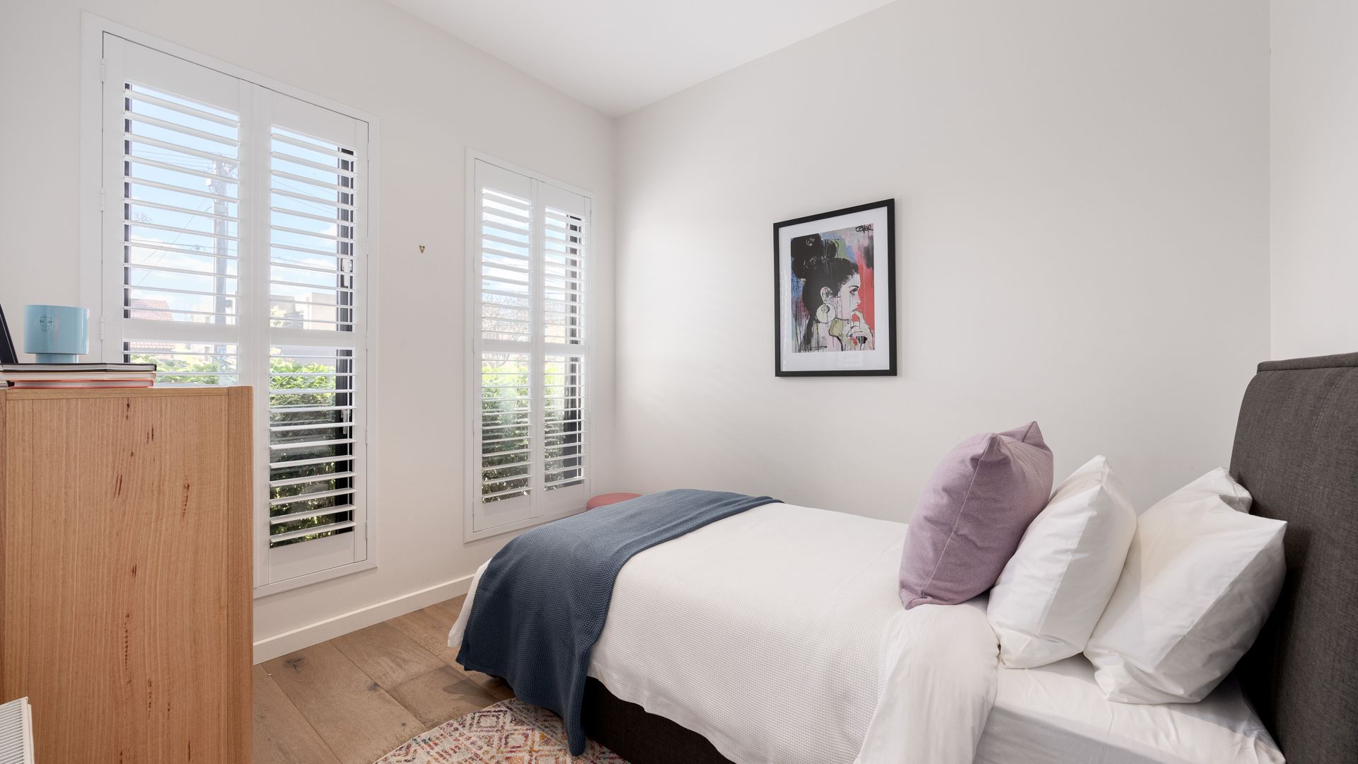 A bedroom with a bed, a bedside table, a wardrobe, and a window with blinds.