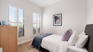 Quarto com cama, mesa de cabeceira, guarda-roupa e janela com persianas.