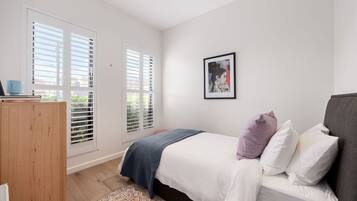 A bedroom with a bed, a bedside table, a wardrobe, and a window with blinds.