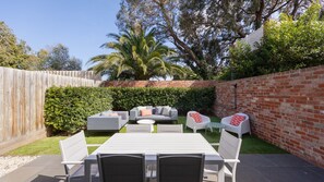 An outdoor patio area with a dining table and chairs, surrounded by a brick wall and a wooden fence. - Arden Green in Caulfield (Caulfield)