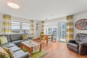 A living room with a sofa, coffee table, and a dining area with a table and chairs. - Holiday apartment with 1 bedroom (Cuxhaven-Sahlenburg)