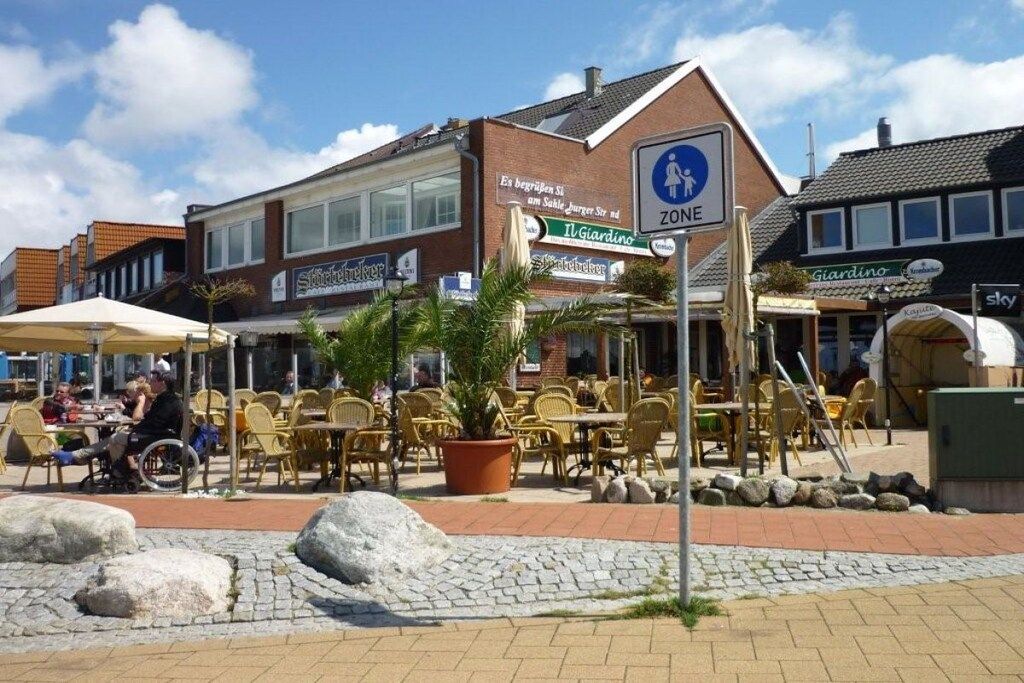 Une place publique avec des sièges en plein air, un panneau indiquant une zone piétonne et un bâtiment avec une enseigne.